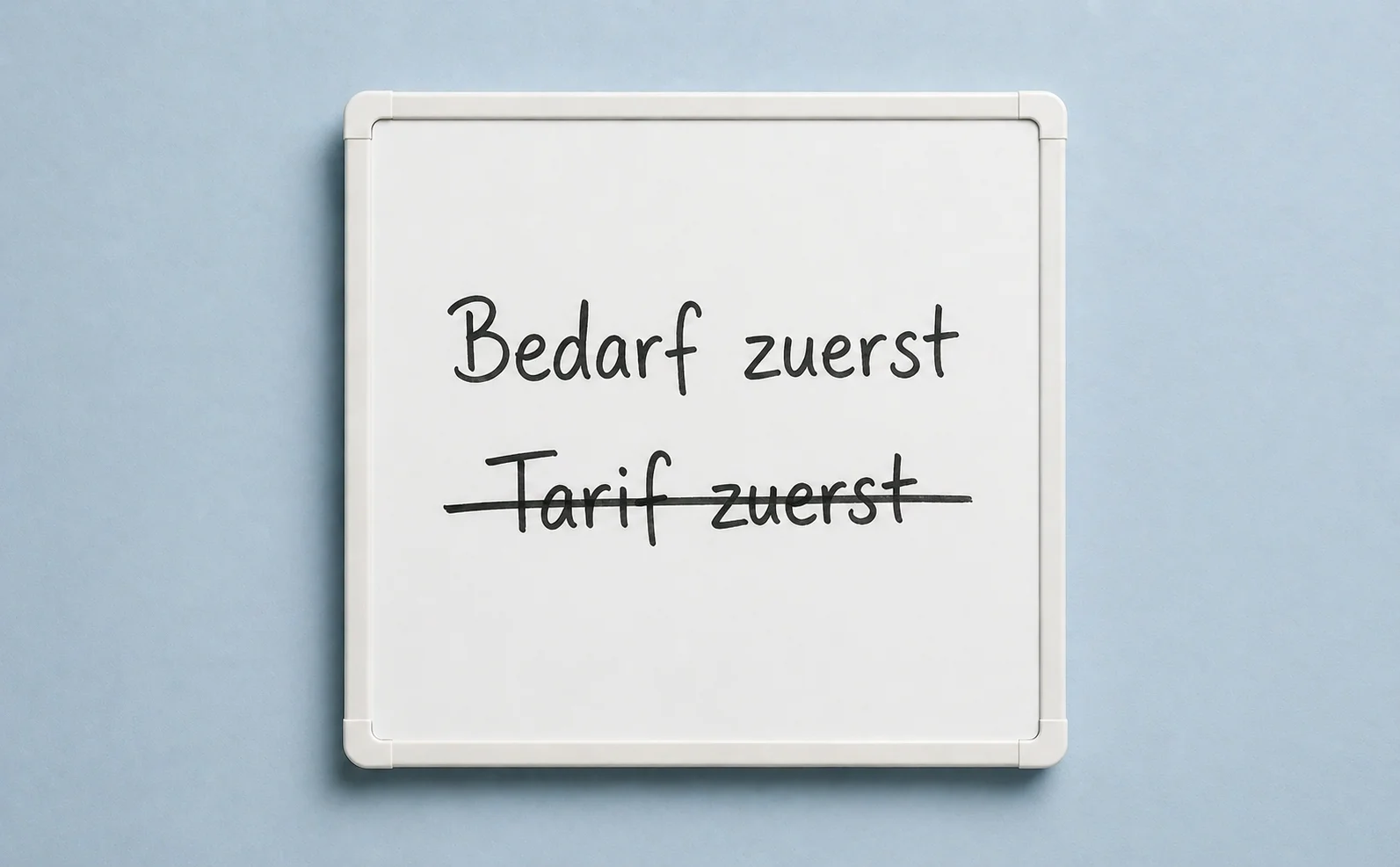 Whiteboard-Detail vor pastell-staubblauem Studio-Hintergrund. Handschriftlich oben Bedarf zuerst, darunter durchgestrichen Tarif zuerst.